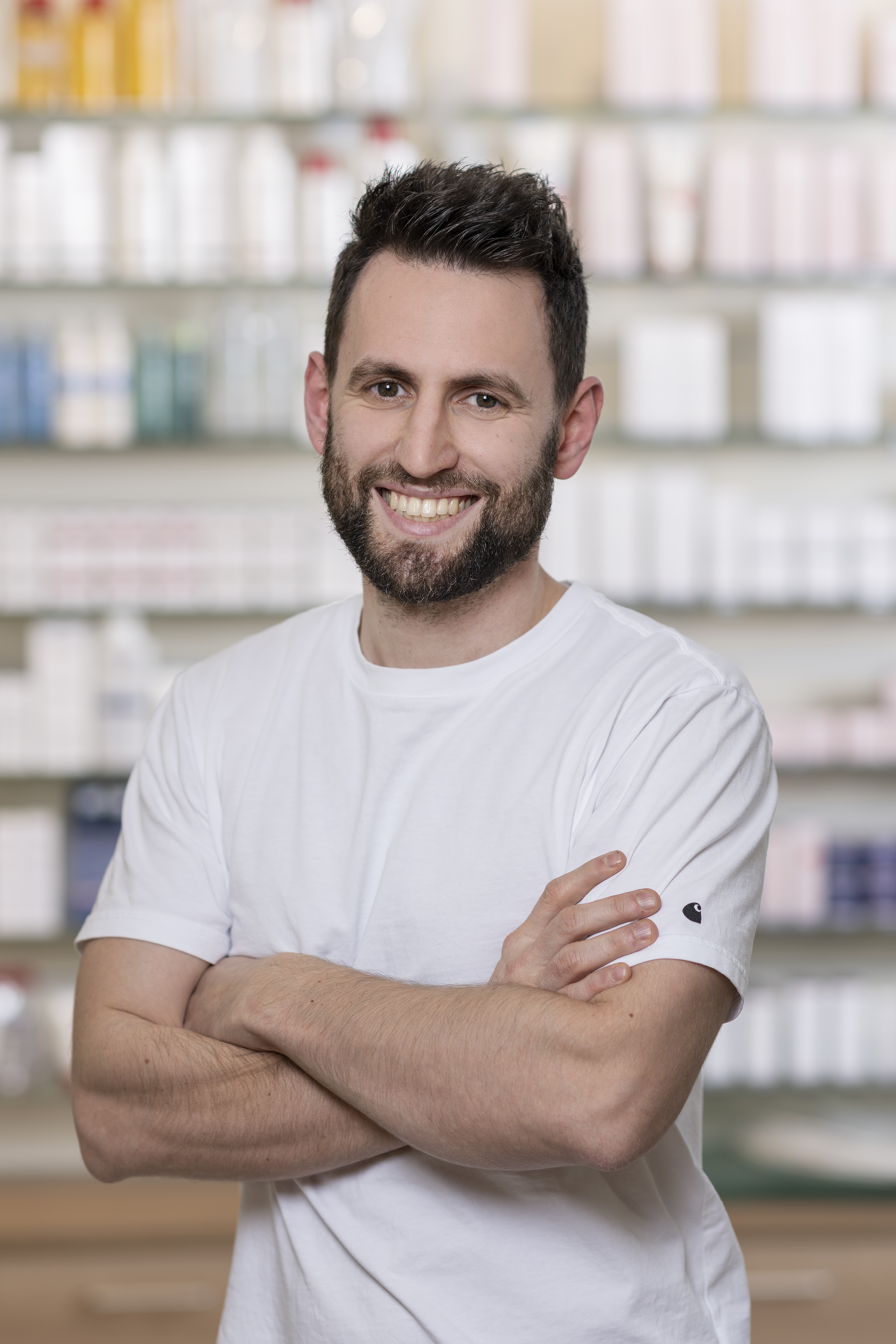 Mitarbeiter der Apotheke Wildschönau steht mit verschränkten Armen lächelnd vor einem Regal mit Produkten.