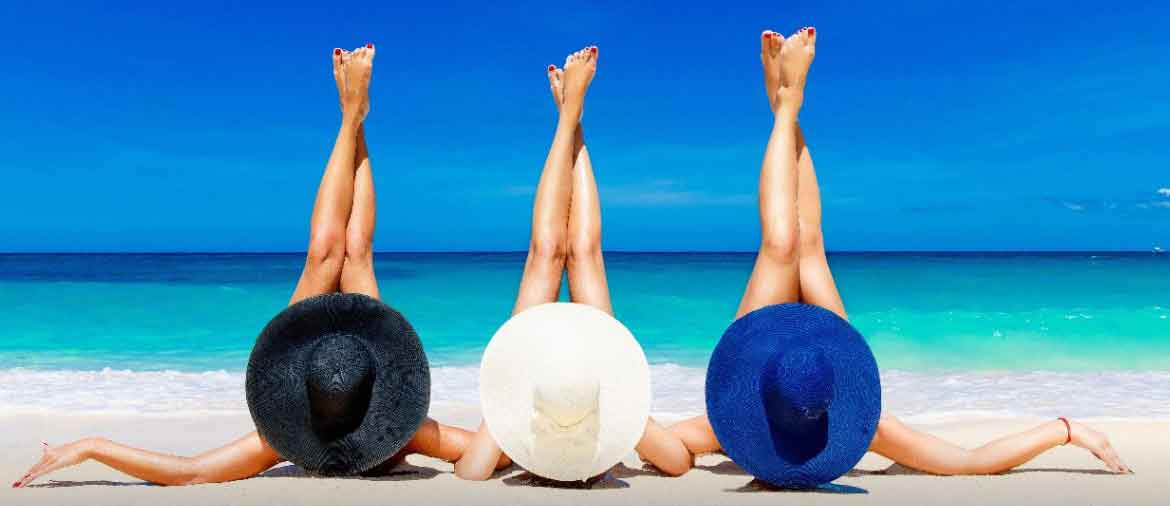 Drei Frauen liegen am Strand mit erhobenen Beinen und großen Sonnenhüten, dazu der Text „Beine erfrischen, entspannen, beleben“.
