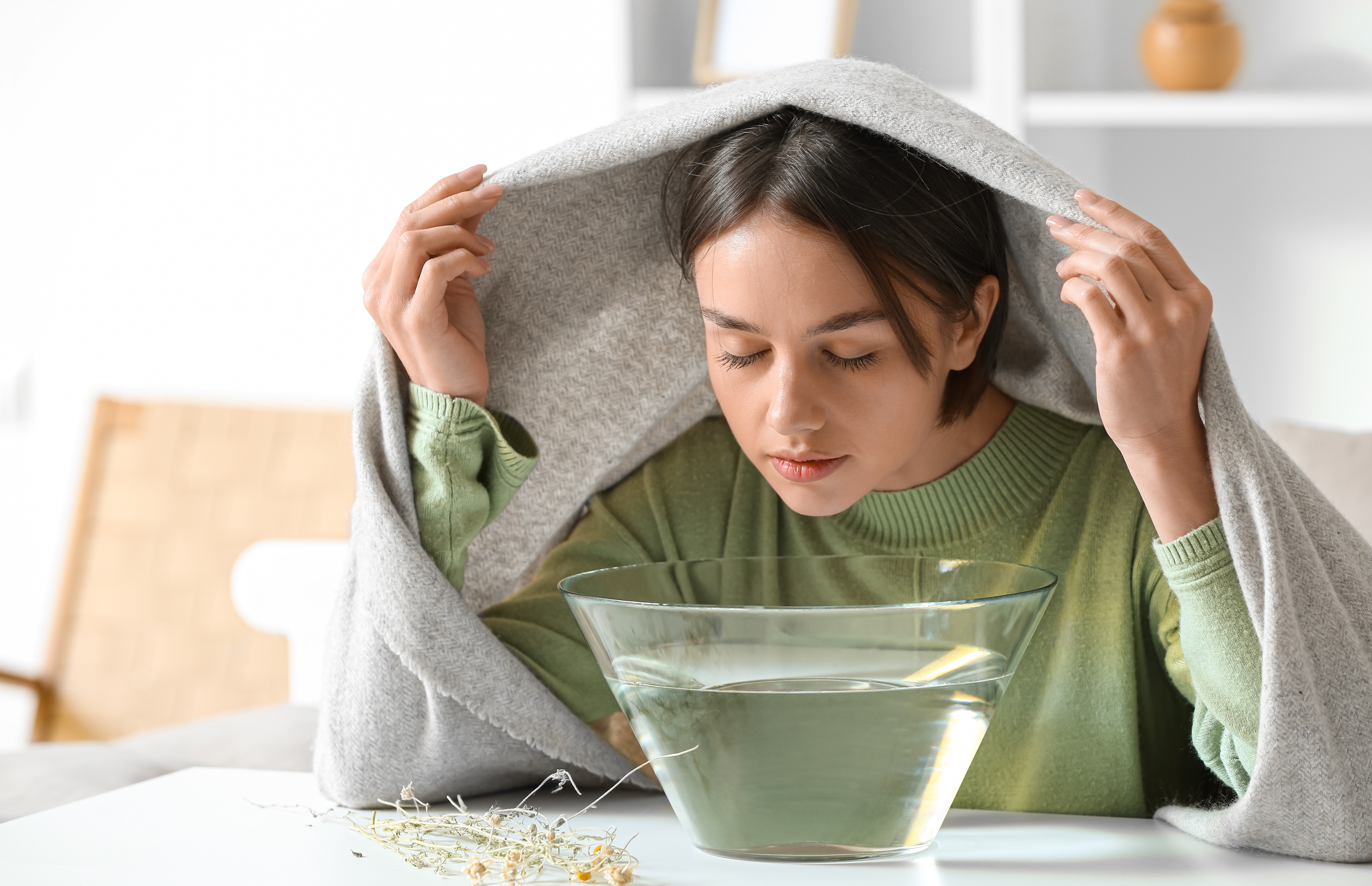 Inhalation bei Erkältung Frau inhaliert Wasserdampf unter einem Handtuch mit einer Schüssel auf dem Tisch zur Linderung bei Erkältung.