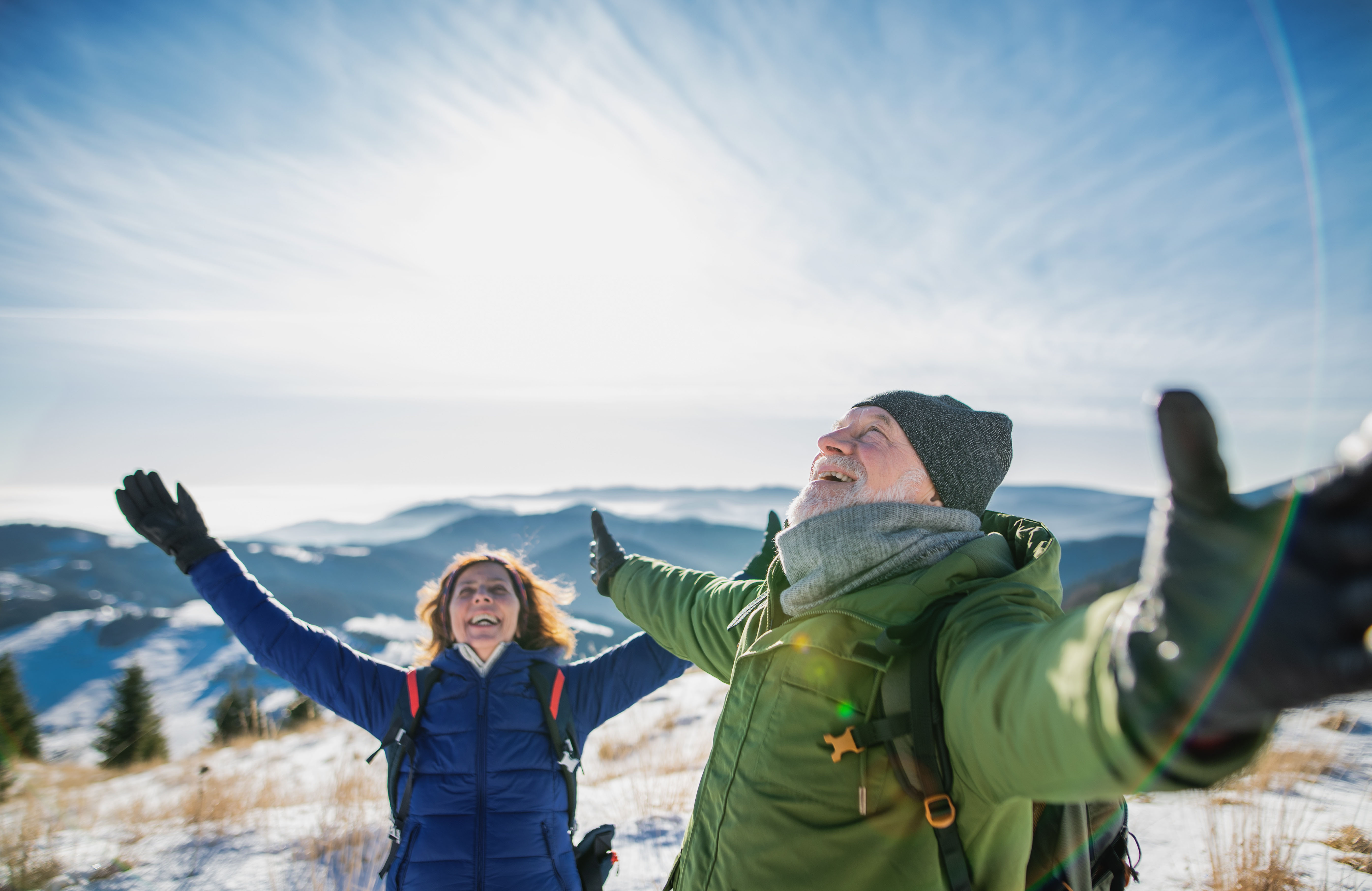 Gesunde Personen biem Wandern Zwei wandernde Personen mit ausgestreckten Armen genießen die frische Luft in verschneiter Berglandschaft.