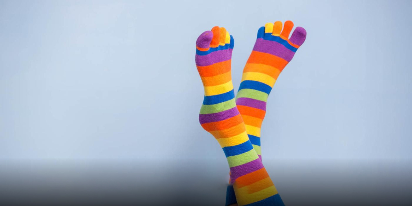Zwei Füße mit gestreiften Zehensocken liegen locker übereinander vor neutralem Hintergrund.