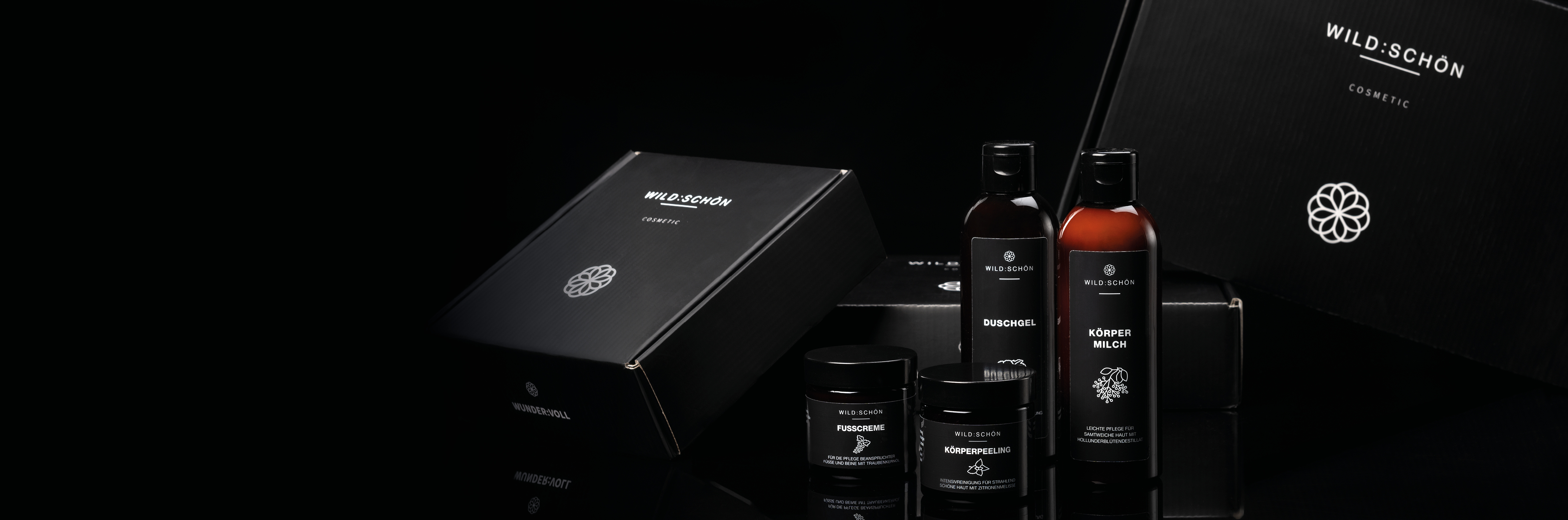 Verschiedene Kosmetikprodukte von WildSchön, darunter Flaschen und Dosen, vor schwarzen Verpackungen.